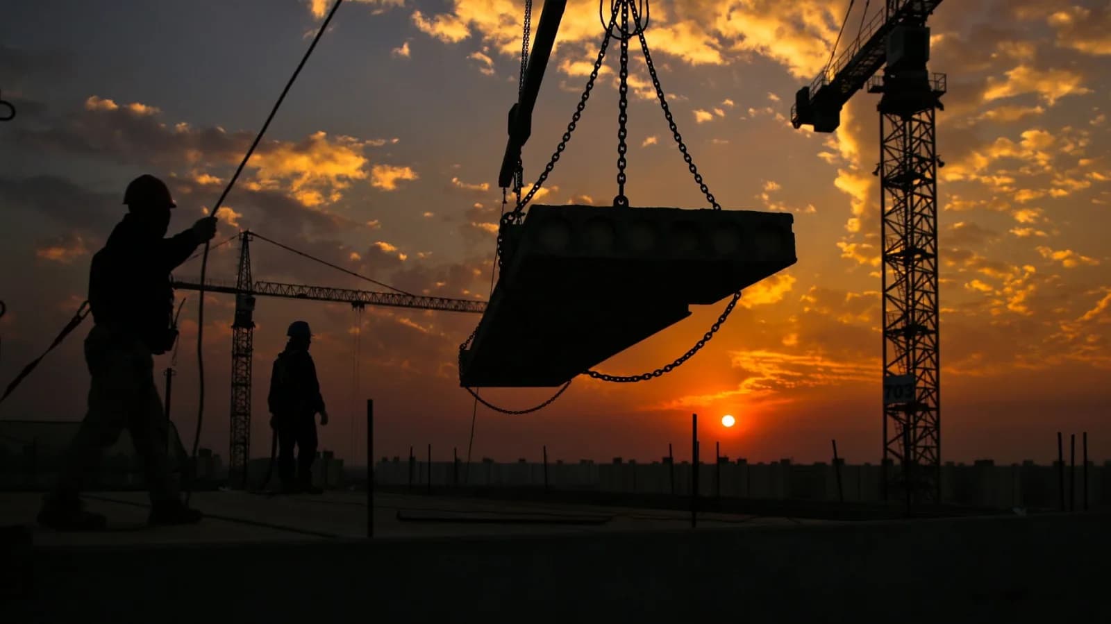 Crane lowering a concrete slab on a construction site at sunset